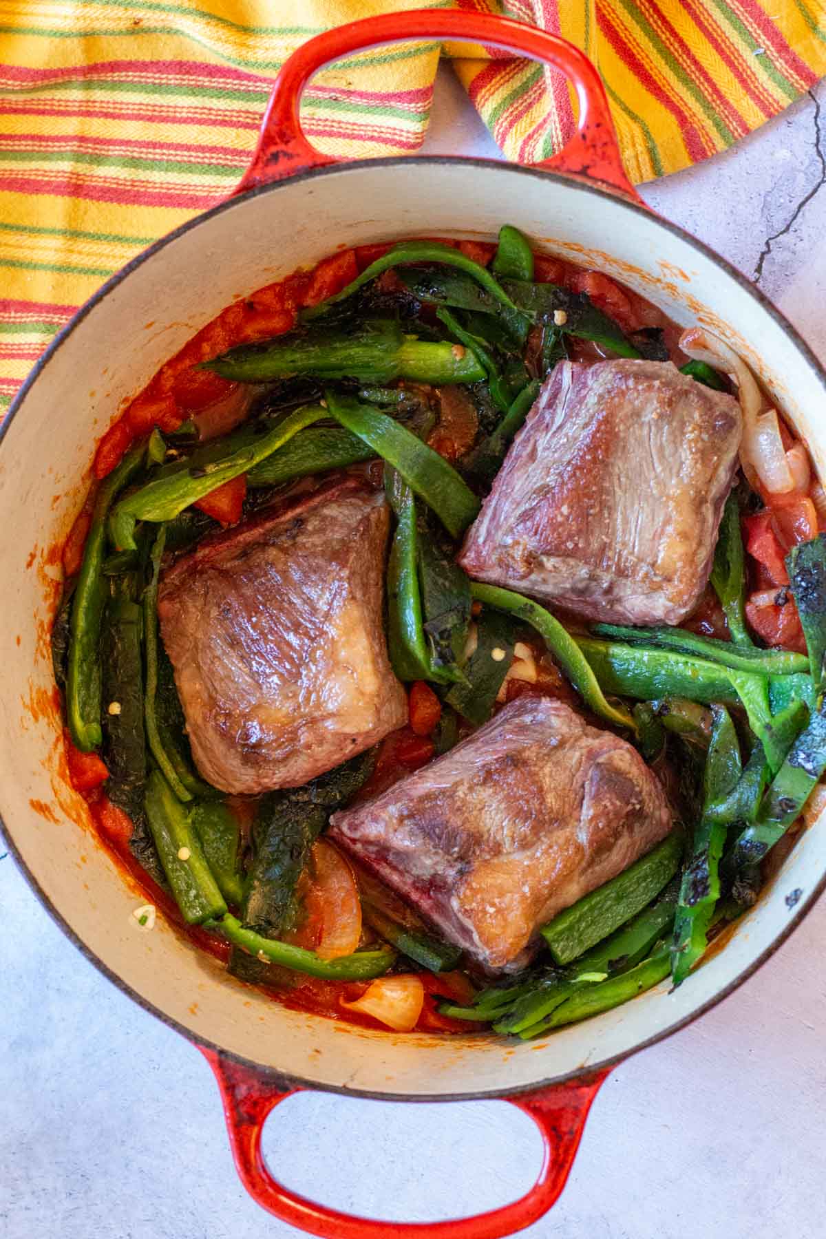 Mexican short ribs in a dutch oven with poblano peppers and tomatoes.