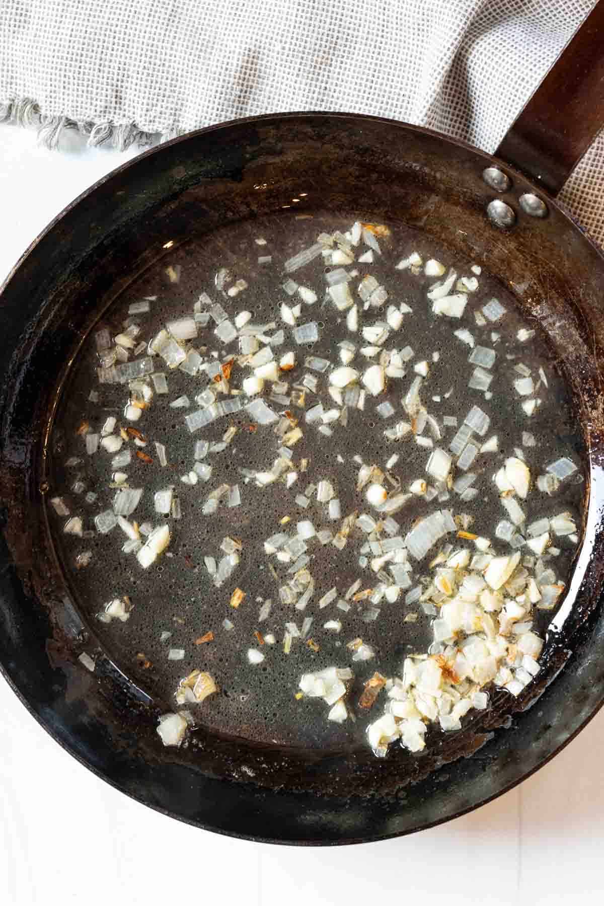 Adding vermouth to shallots and garlic to make shrimp scallop pasta sauce.