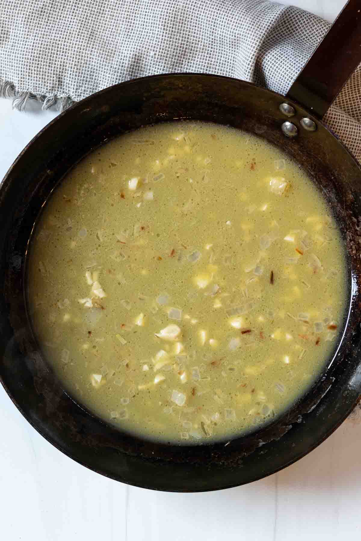 Adding orange juice to pan ingredients to make shrimp scallop pasta sauce.