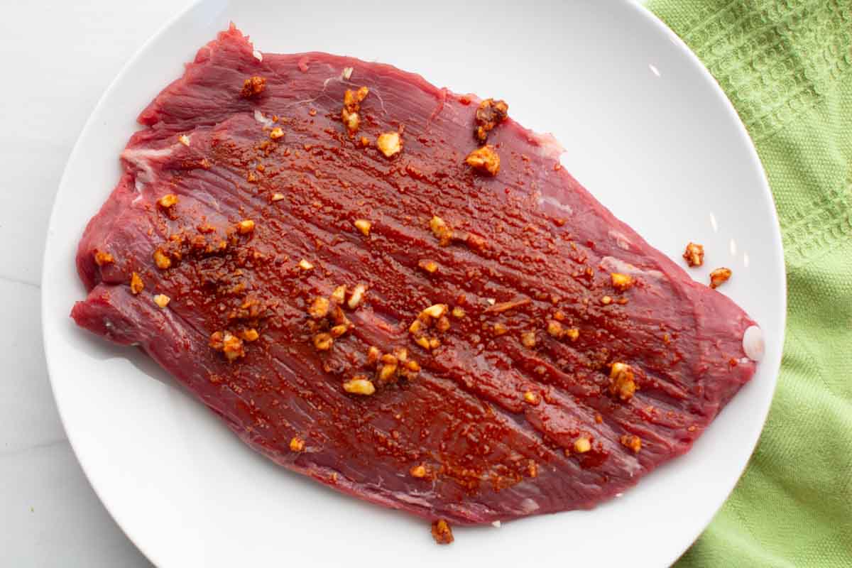 Seasoning flank steak to cook in a cast iron skillet.