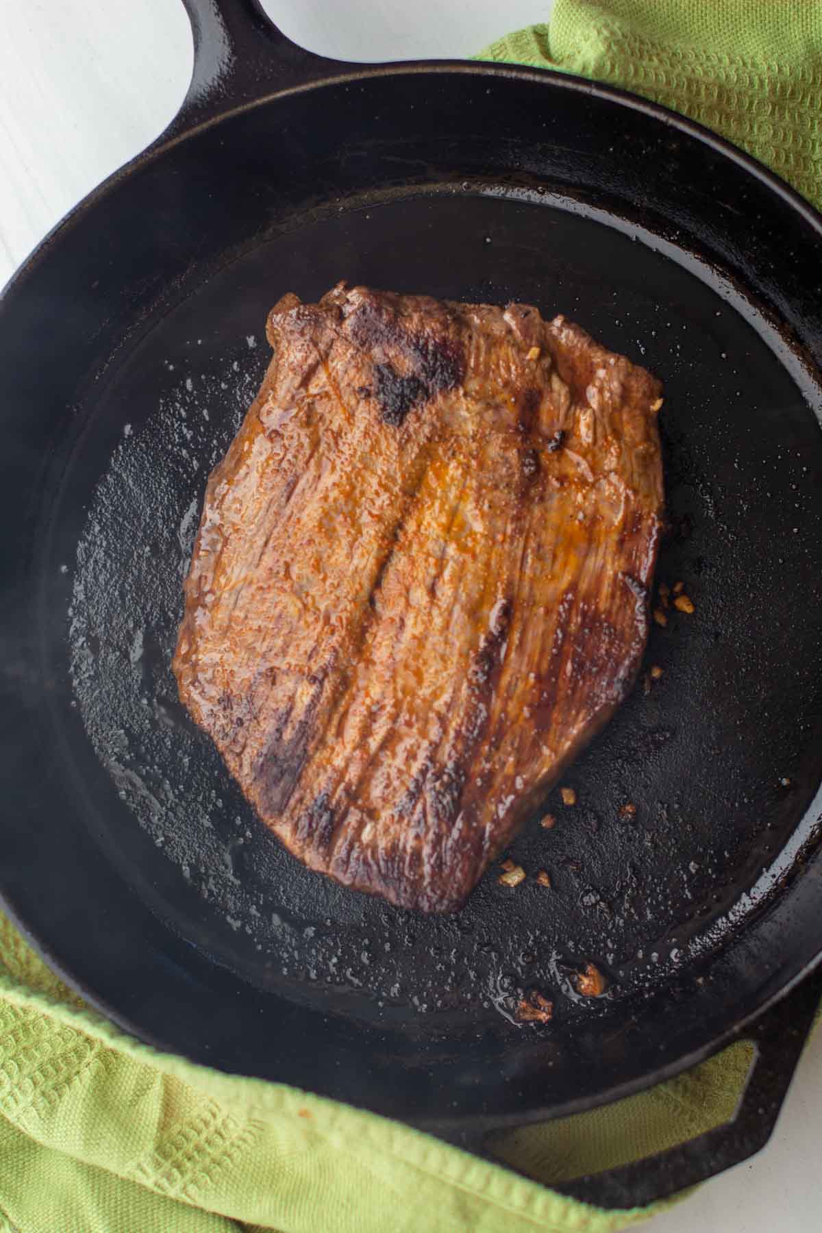 Cooking side two of a flank steak in a cast iron skillet.