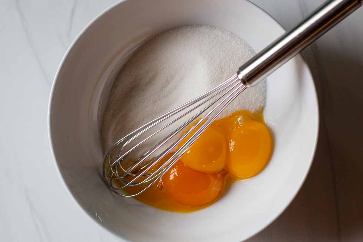 Two egg yolks and sugar in a bowl.