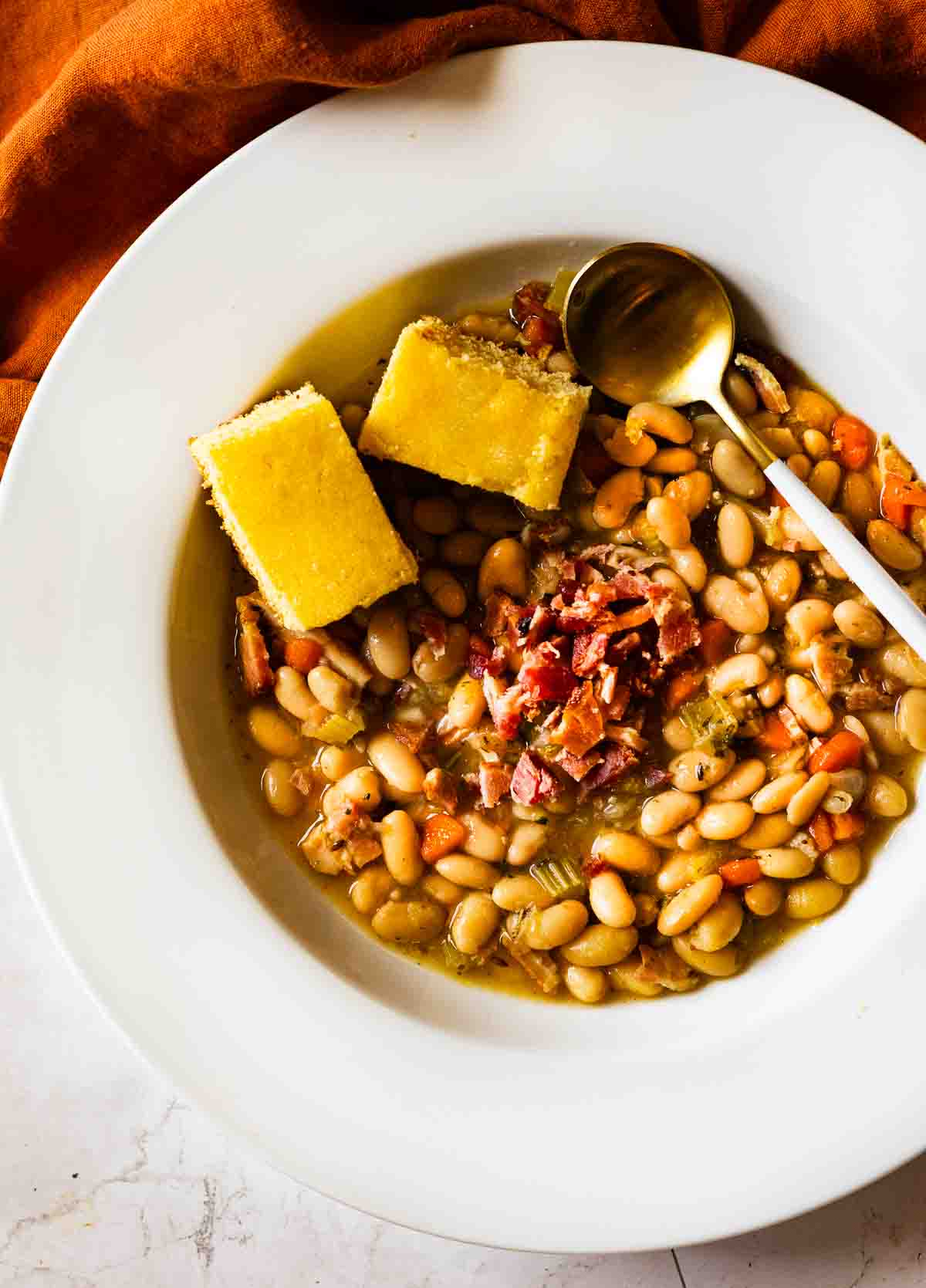 A bowl of great northern bean soup topped with bacon bits and two slices of cornbread.