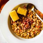 A bowl of great Northern bean soup topped with corn bread and bacon.