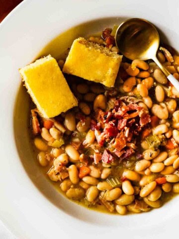 A bowl of great Northern bean soup topped with corn bread and bacon.