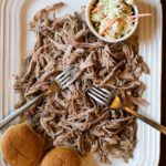 A platter of pulled pork with cole slaw and buns