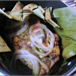 Achiote Paste Shredded Pork Tacos wrapped in banana leaves and topped with onions.