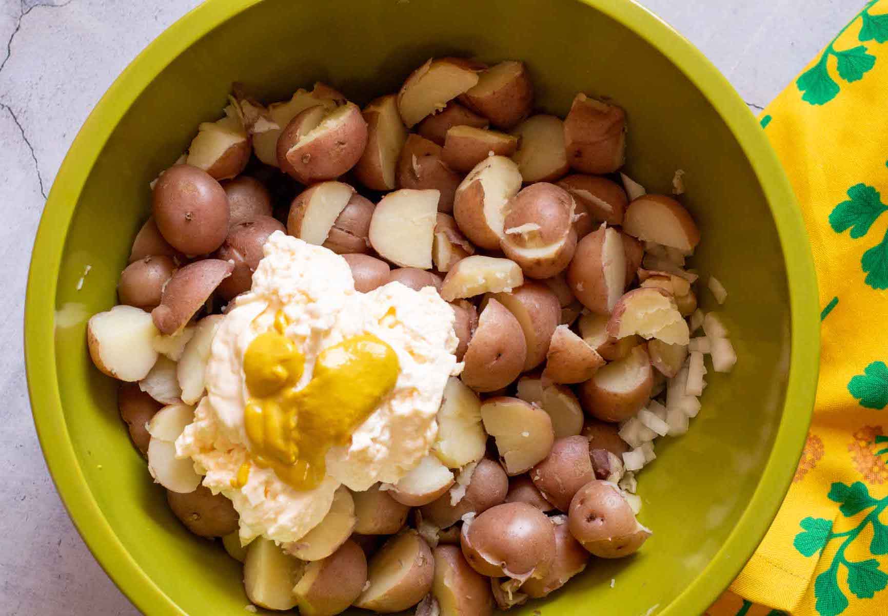 Adding mustard and mayo to red potatoes to make old fashioned potato salad.