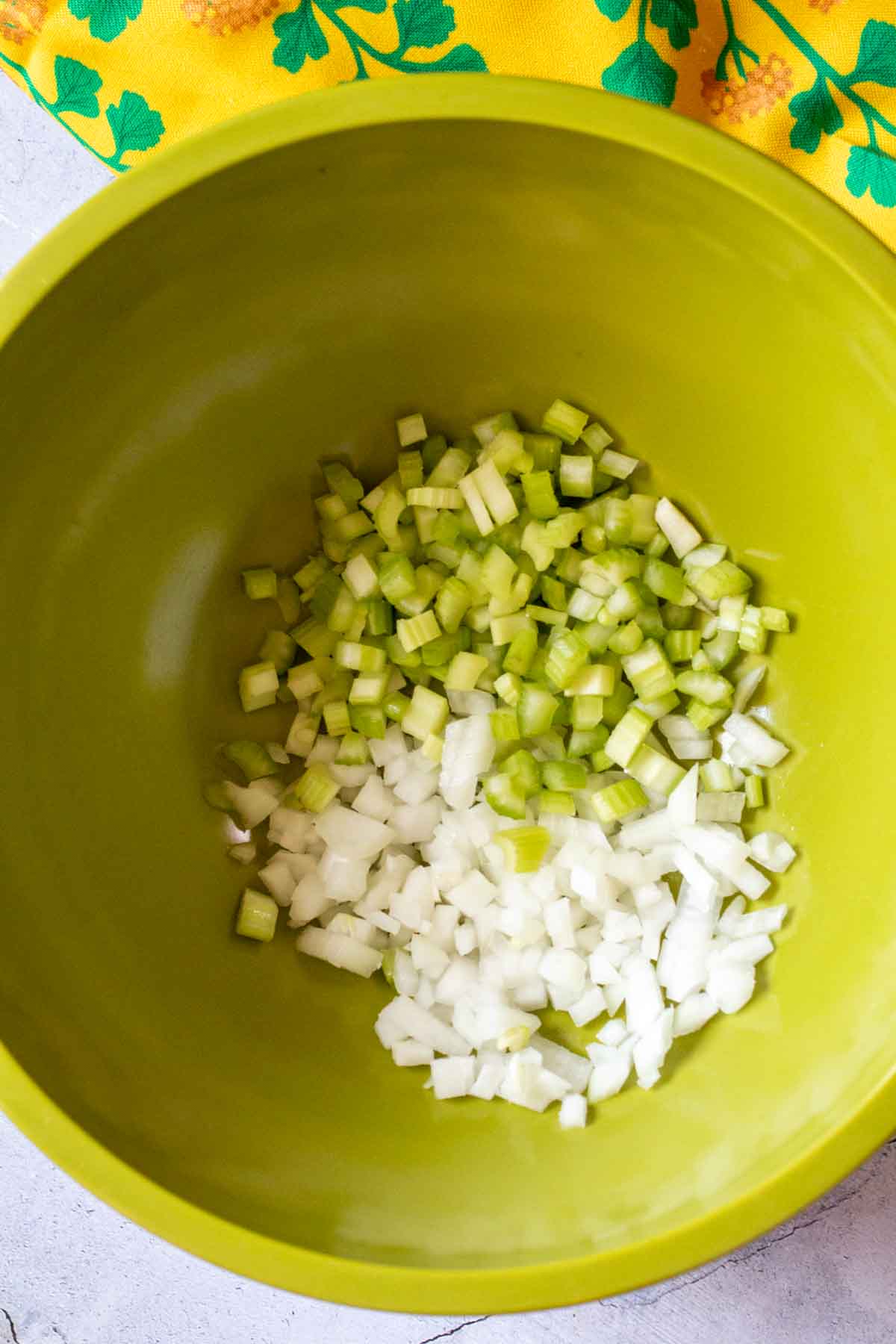 Chopped onion and celery in a large green bowl to make old fashioned potato salad.
