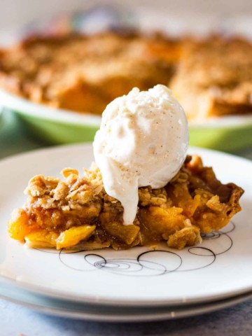 A slice of peach crumble pie topped with a scoop of vanilla ice cream.