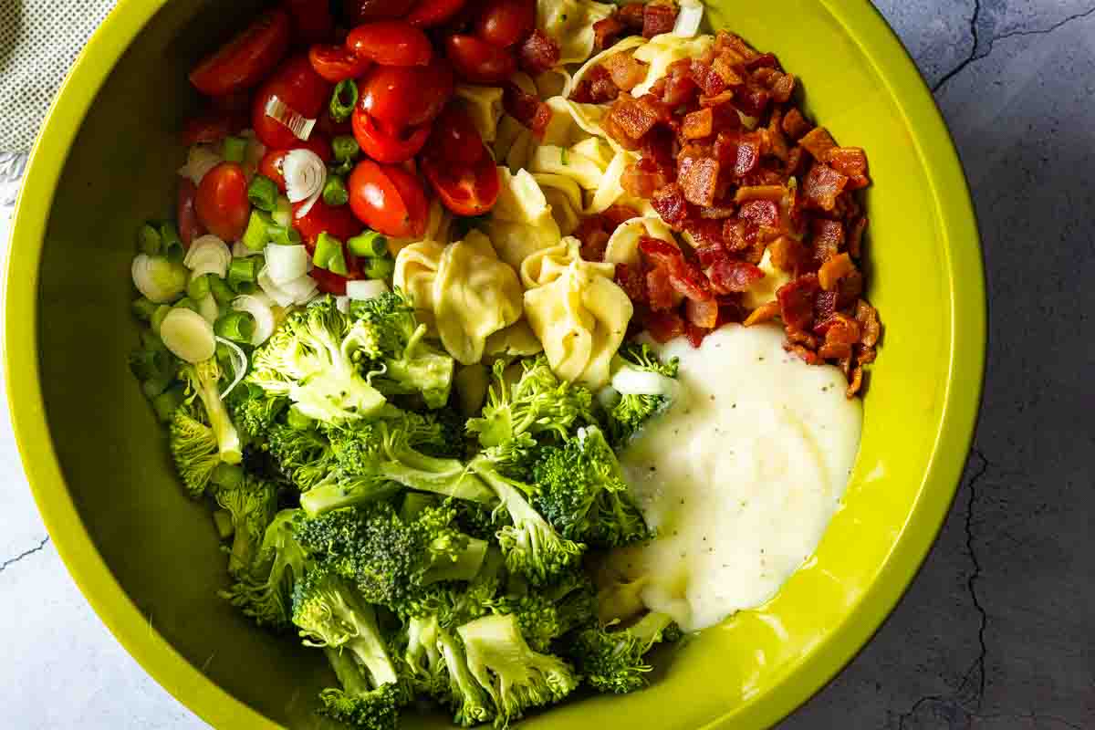 Adding ingredients to cooked cheese tortellini to make Cheese Tortellini Pasta Salad.