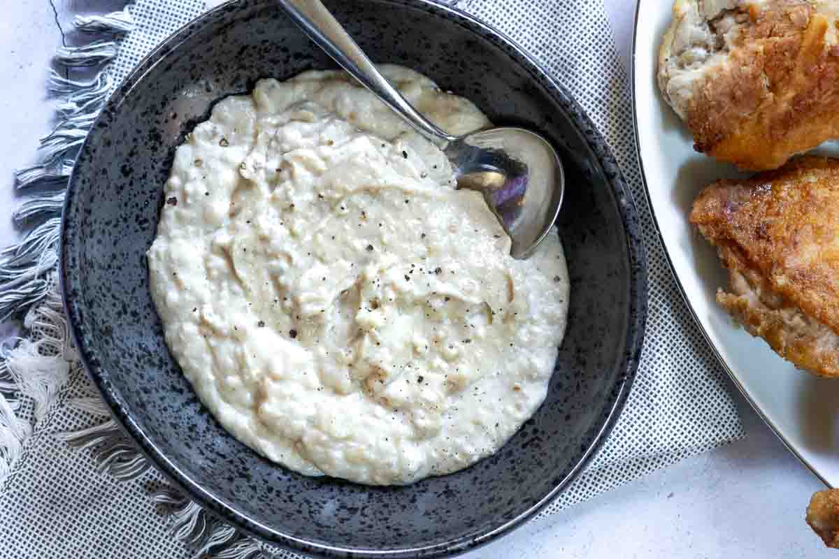 Fried chicken gravy in a black bowl with a ladle for serving.