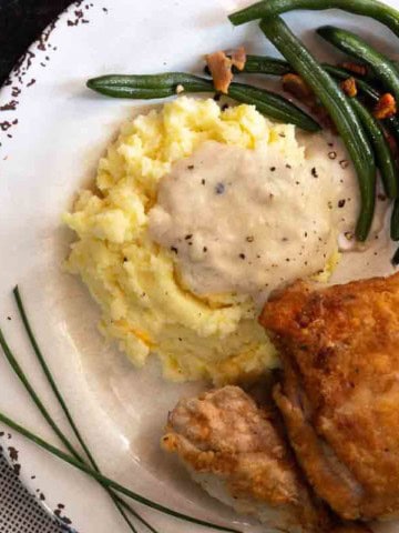 Pan fried chicken with potatoes and fried chicken gravy served with green beans.