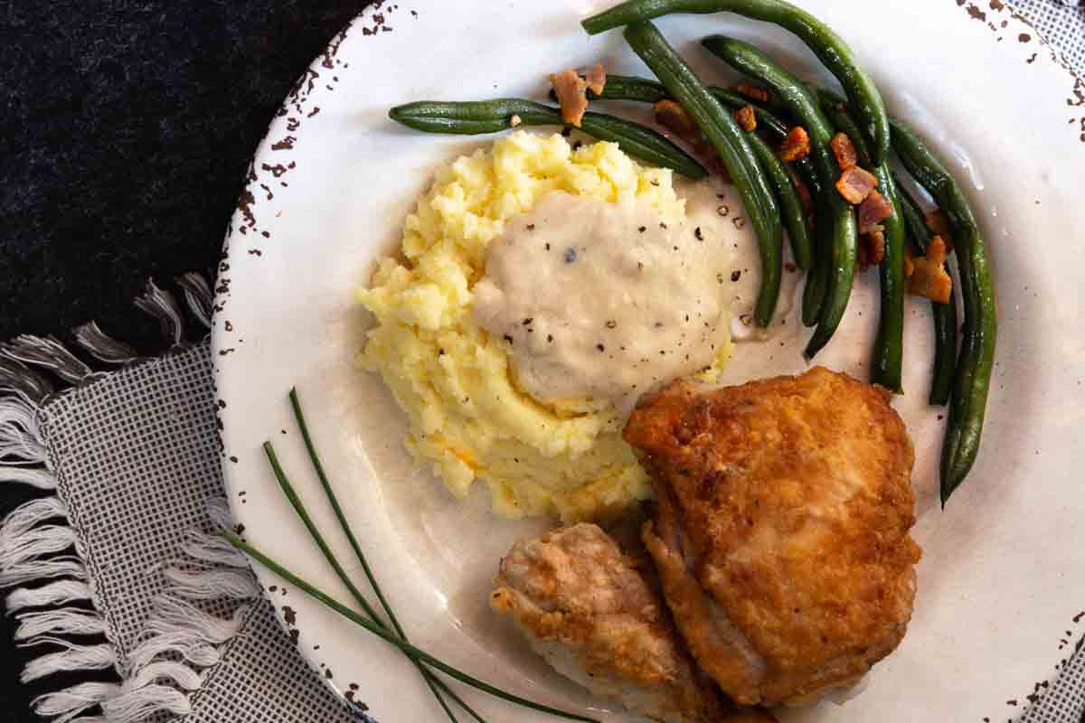 Pan fried chicken with potatoes and fried chicken gravy served with green beans.