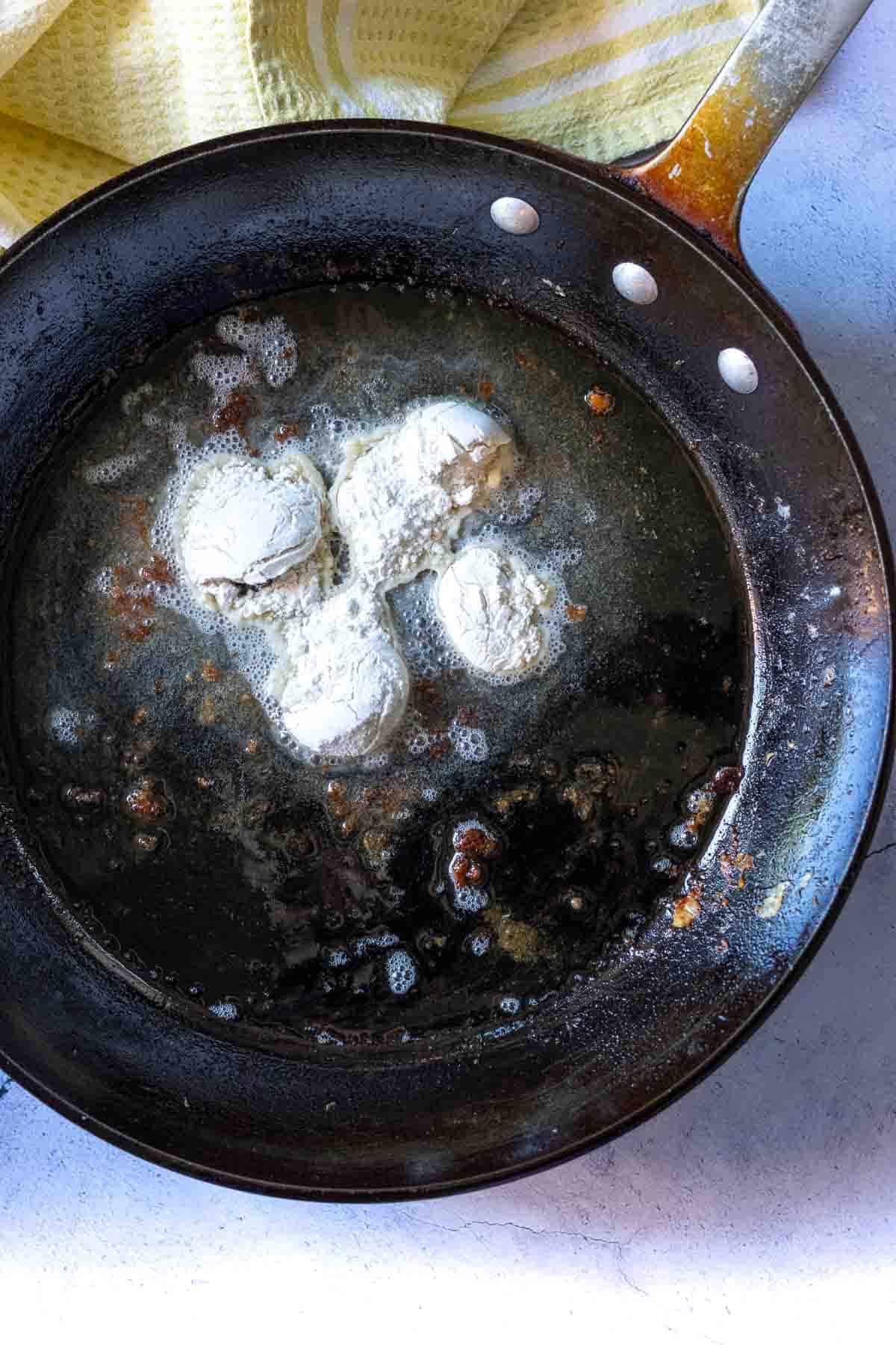 Adding flour to oil in frying pan to make fried chicken gravy.