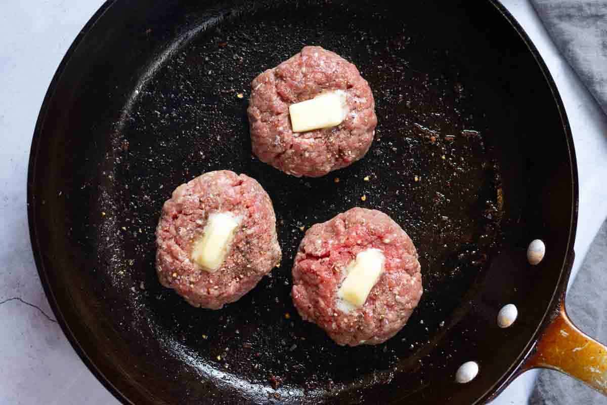 Pan frying BLT Burgers with a pat of butter on top of each.