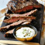 Best Flank Steak Marinade flank steak on a dark wooden board with horseradish cream
