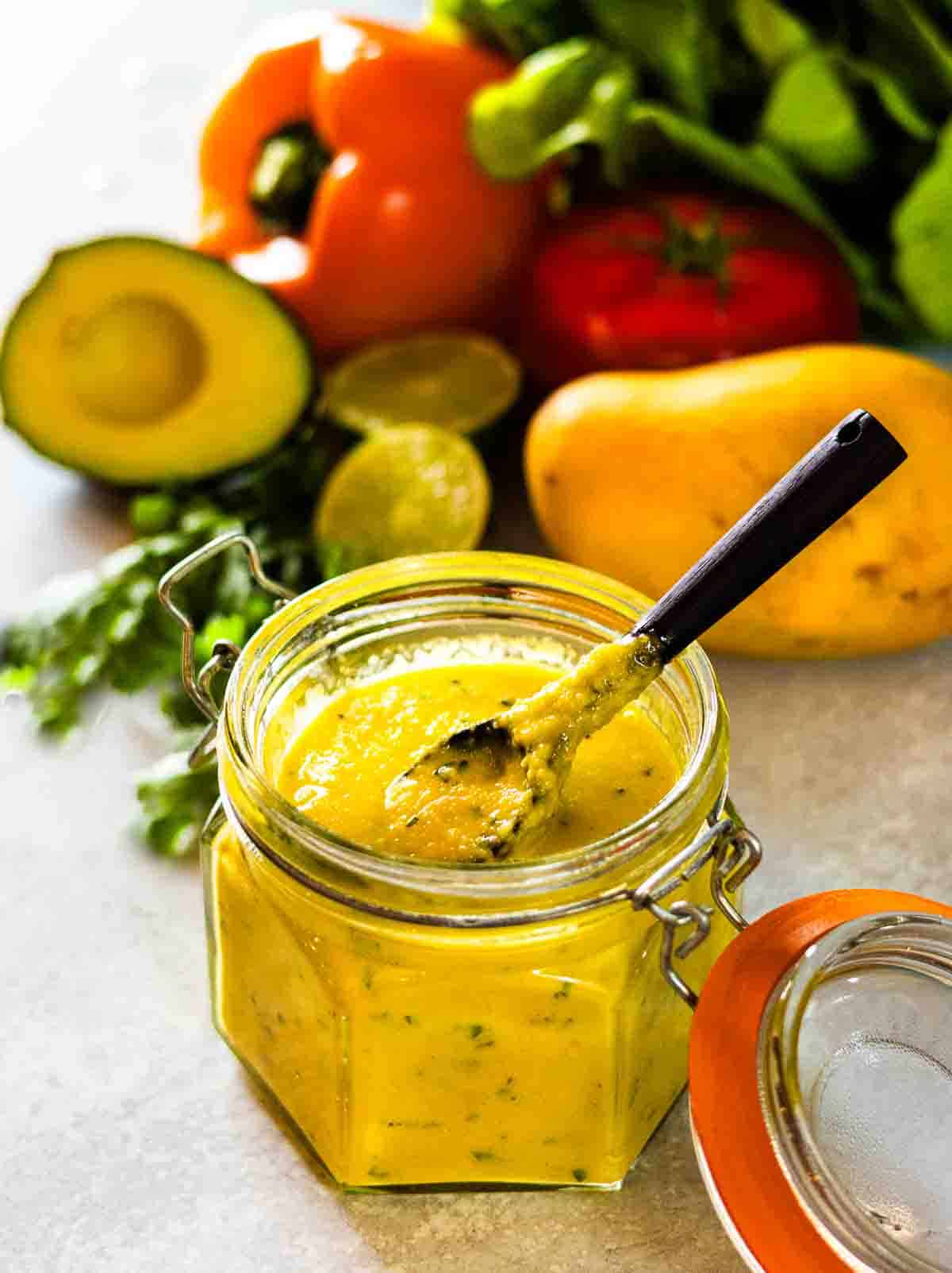 A jar of mango dressing with salad ingredients behind.