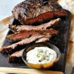 Grilled flank steak on a cutting board with tangy horseradish sauce.