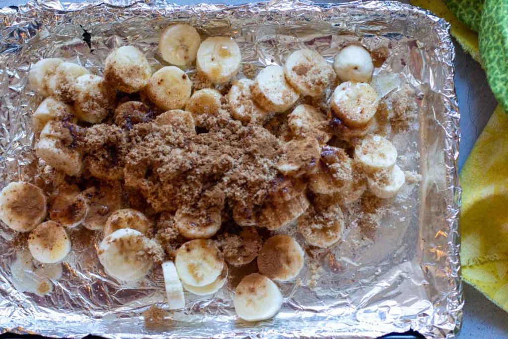 Sliced bananas on a foil lined sheet pan sprinkled with brown sugar and cinnamon.