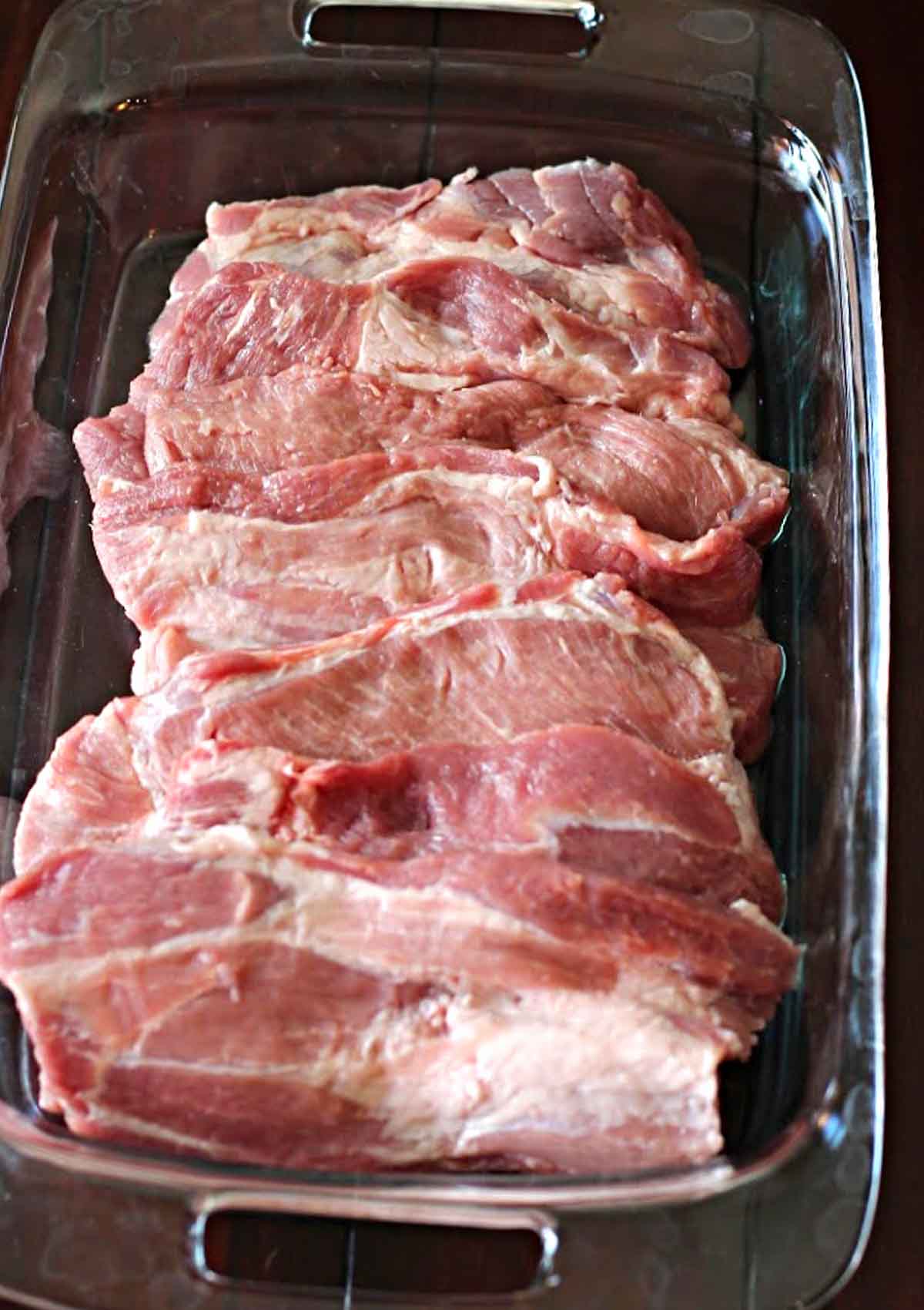 Hand cut pork steaks from a pork shoulder roast in a pyrex baking dish.