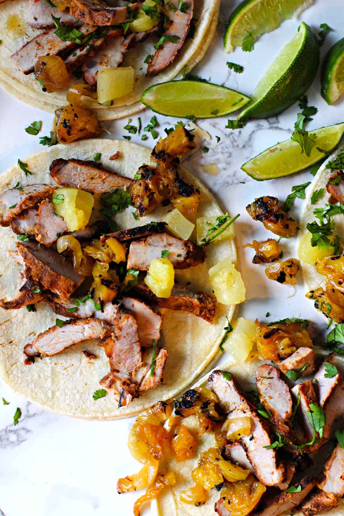 Pork tacos al pastor with pineapple lime wedges on corn tortillas