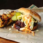 Bobby Flay Texas Burger topped with cole slaw and BBQ sauce served with grilled corn