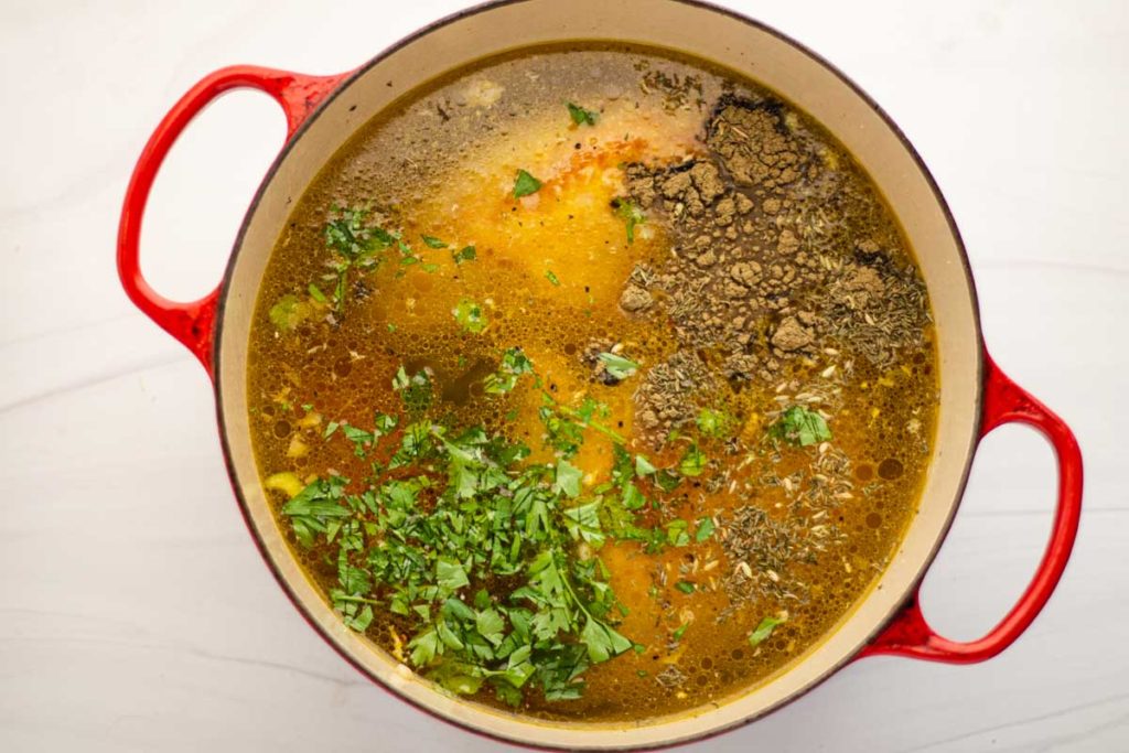 Adding seasonings and broth to chicken soup
