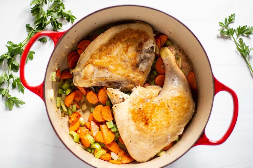 Adding chicken pieces to vegetables to make chicken noodle soup