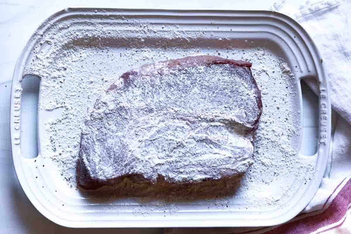 Flouring a chuck roast to make pot roast dinner.
