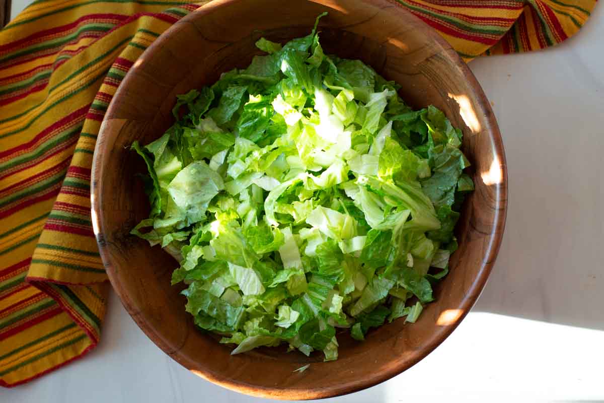Chopped romaine lettuce and iceberg lettuce in a large wooden salad bowl.