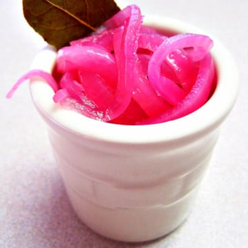 Pickled Red Onions in a white crock jar with a bay leaf