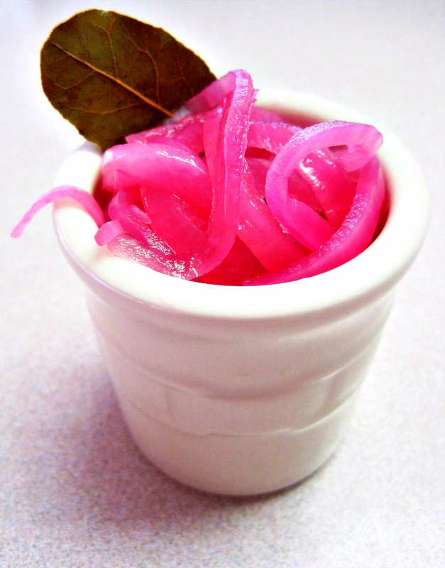 Pickled Red Onions in a white crock jar with a bay leaf