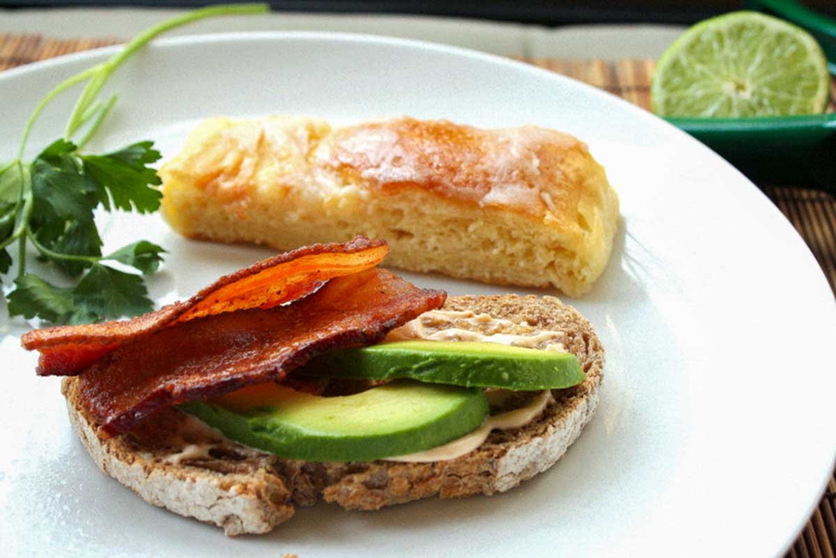 Rustic bread toast topped with bacon and sliced avocado.