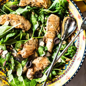 Wilted spinach salad with grilled chicken tenders in a salad bowl.