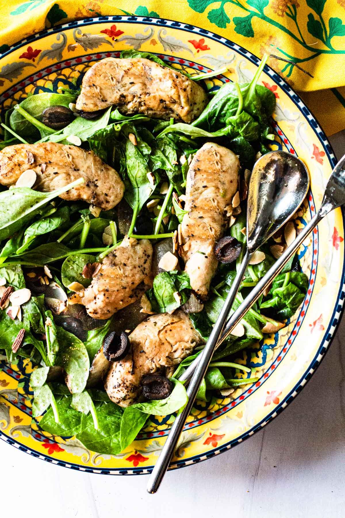 Wilted spinach salad with grilled chicken tenders in a salad bowl.