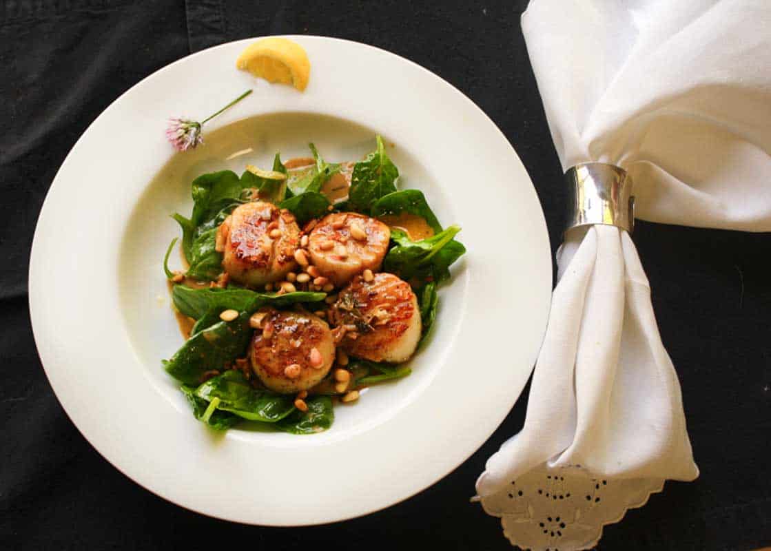 Seared scallops with wine wine butter sauce served over spinach.