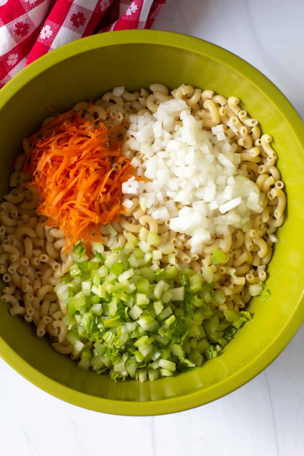 Adding onion, celery and carrot to macaroni noodles.