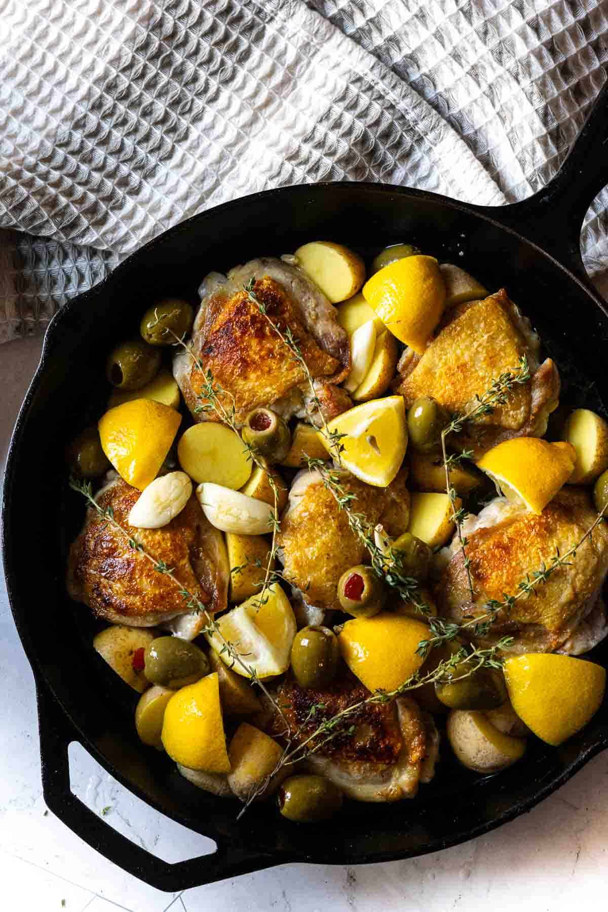 Adding olives and thyme to skillet to make braised chicken thighs.