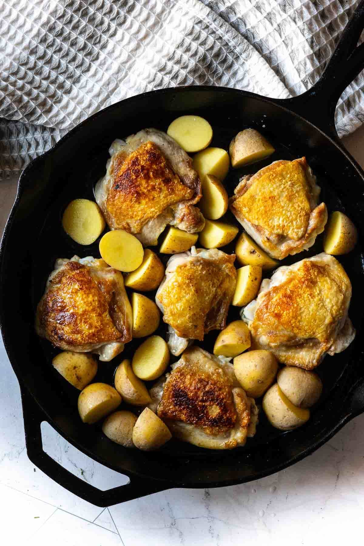 Adding potatoes to a skillet of fried chicken thighs to make braised chicken thighs.