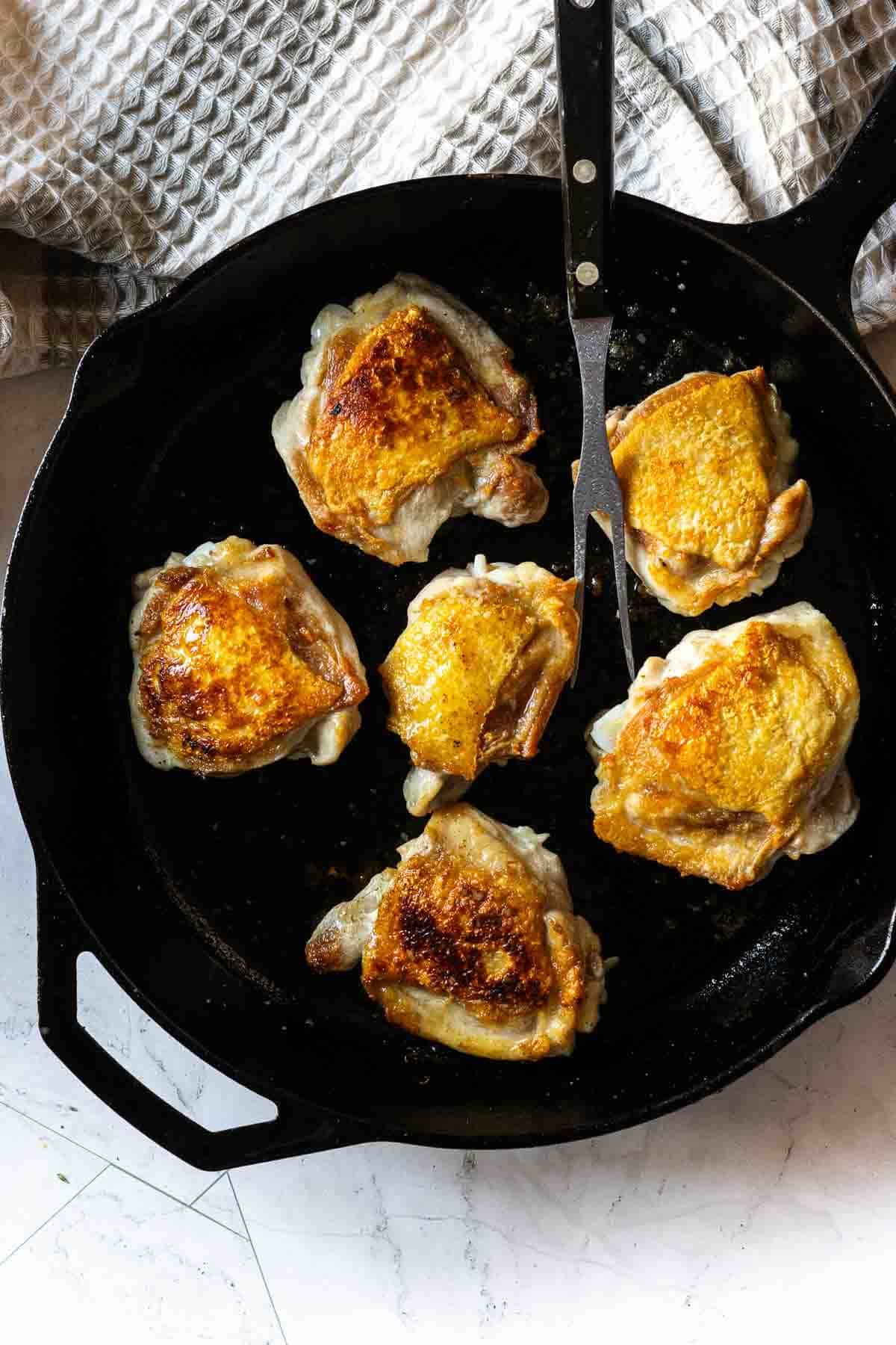 Frying chicken thighs in a cast iron skillet to make braised chicken thighs.