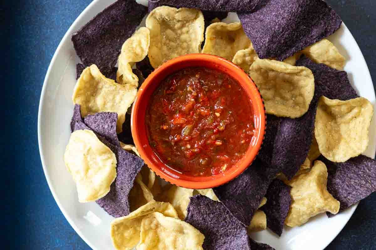 Freezer salsa in a Mexican bowl surrounded by blue and white corn chips.