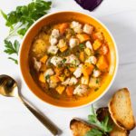 Chicken soup with sweet potatoes garnished with fresh parsley and toasted baguette