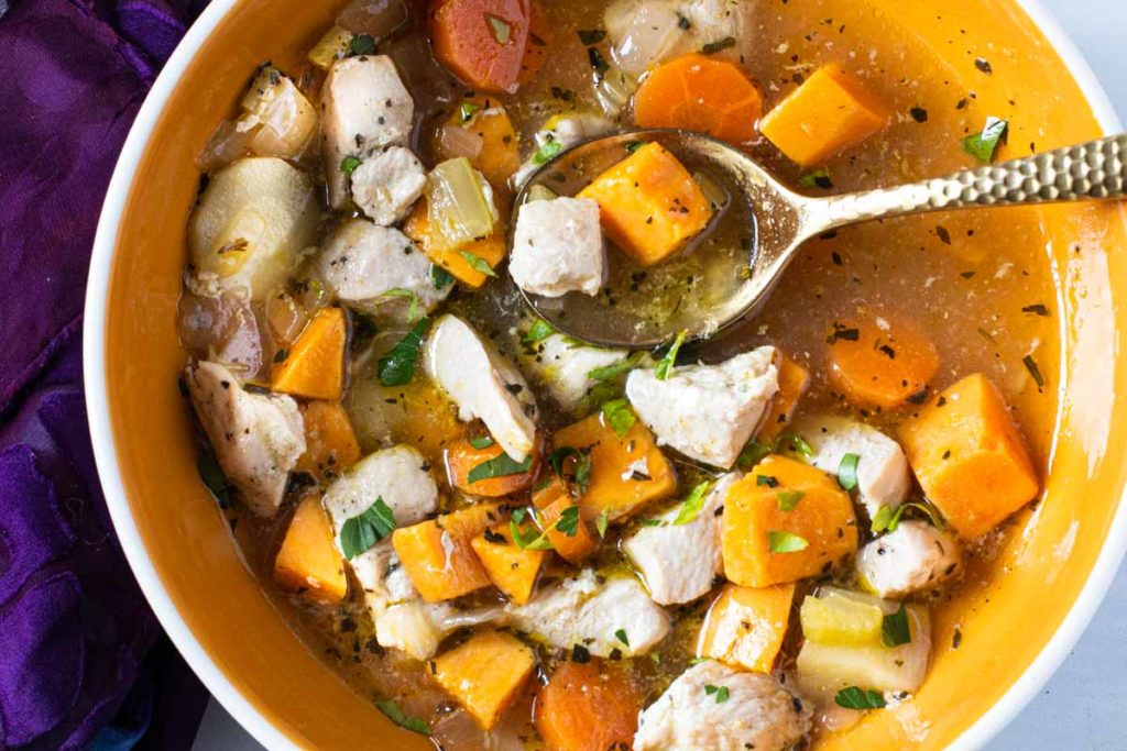 Chicken soup with sweet potatoes in an orange bowl with a gold spoon