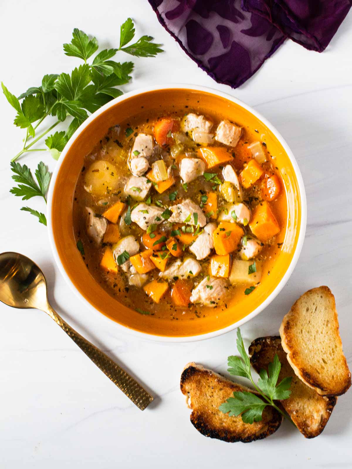 Chicken soup with sweet potatoes garnished with fresh parsley and toasted baguette