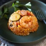 Spicy paella with shrimp and sausage on a blue plate.