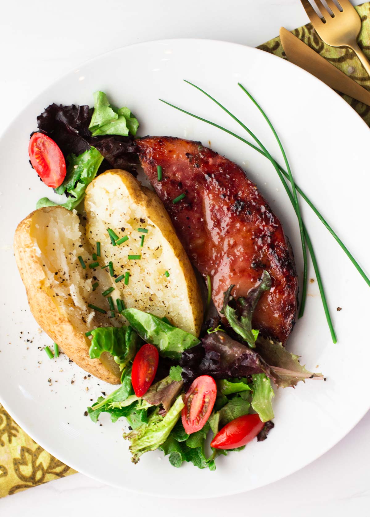 Glazed grilled ham steak with baked potato and lettuce salad garnished with chives
