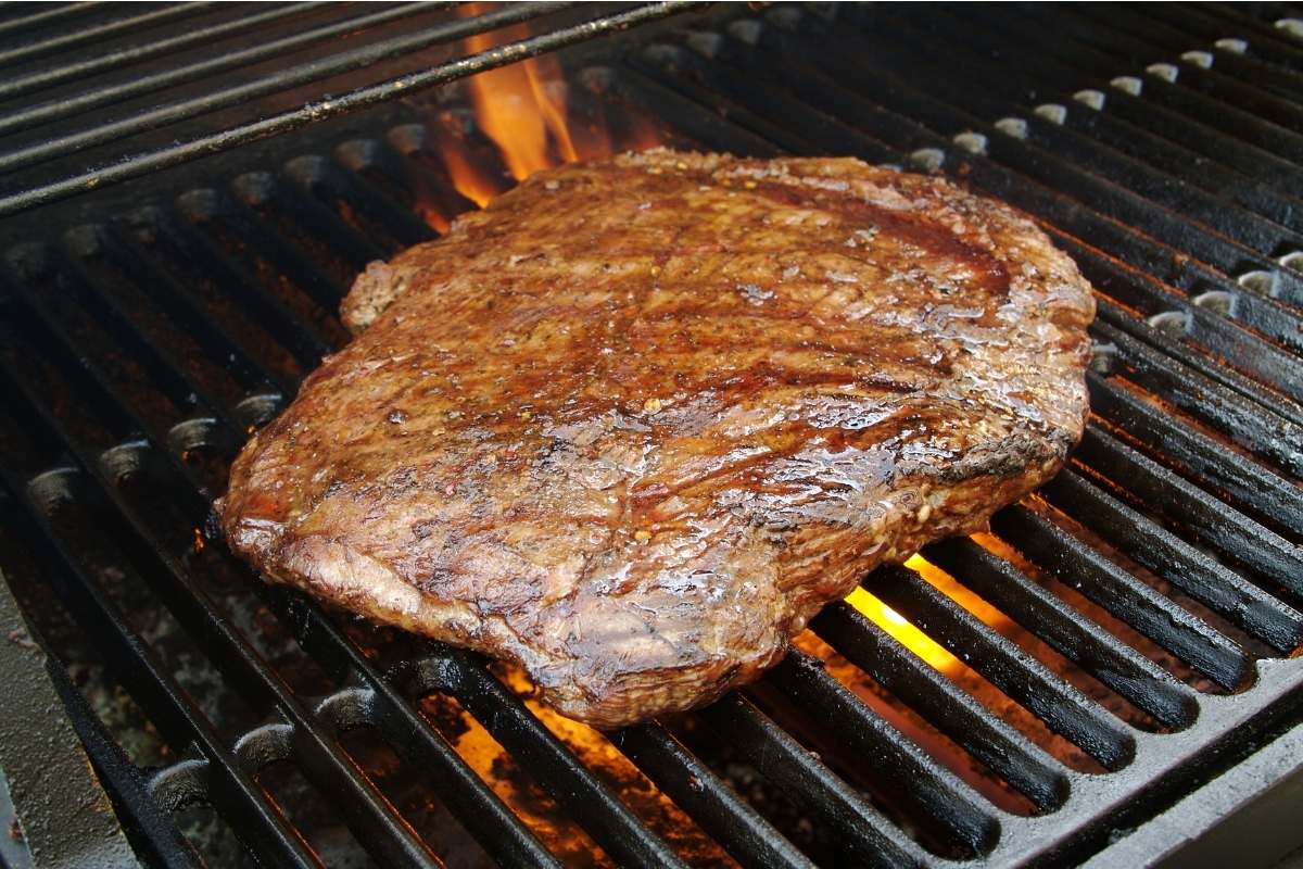Flank steak being grilled on a gas grill.