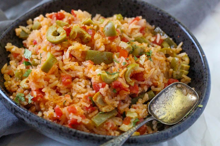 Spanish Green Rice served in a black bowl topped with green olives and red chile powder