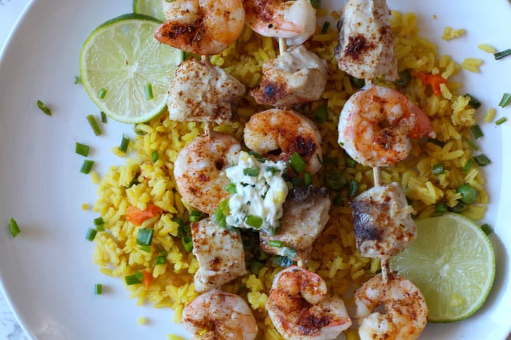 Shrimp and Mahi Mahi on wooden skewers served on yellow Mexican rice, topped with a dollop of jalapeno butter and garnished with chives and lime slices